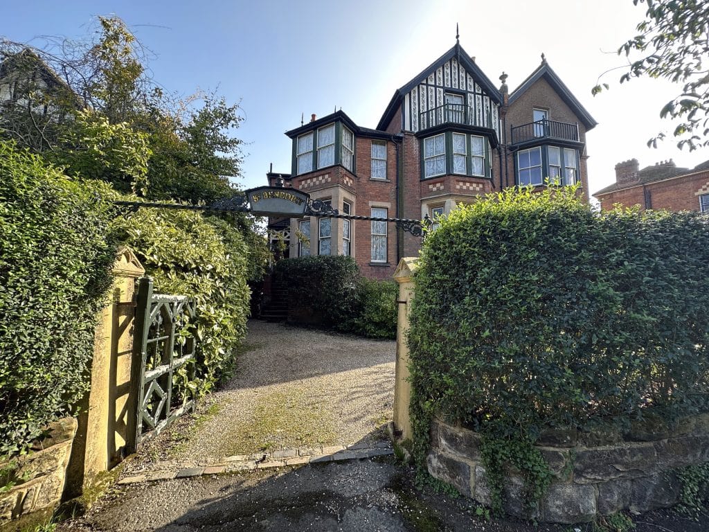 a house with bushes in front of a brick building with Moseley Old Hall in the background
